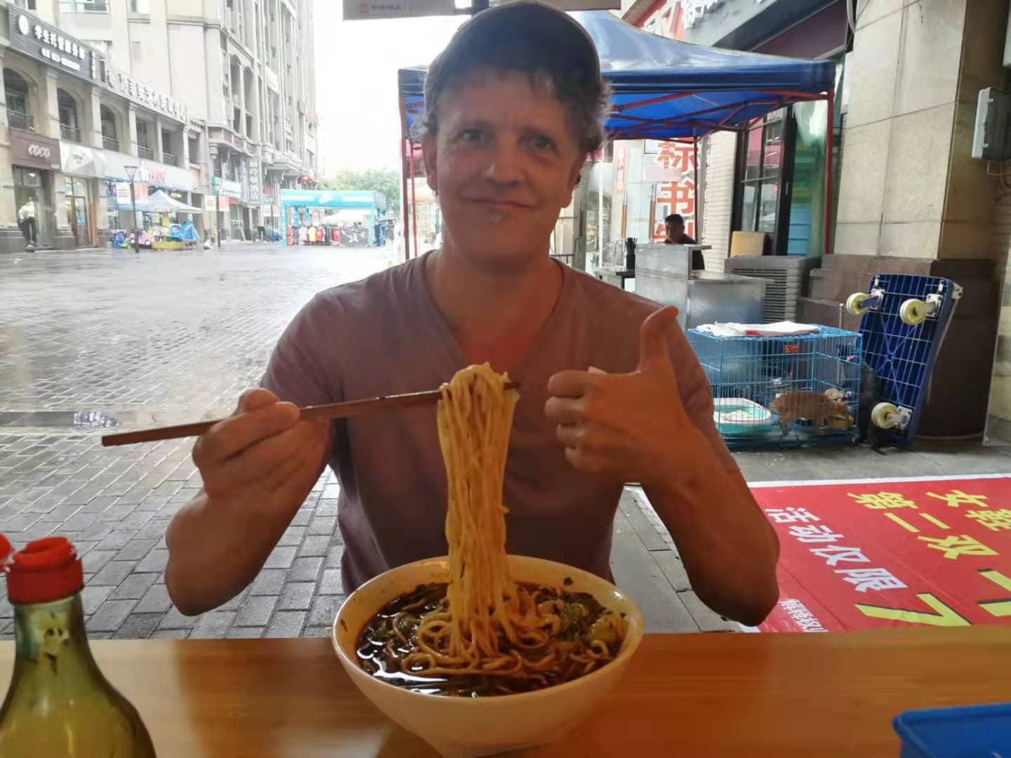 Jaime Terauds at a street-side table in China, holding noodles with chopsticks